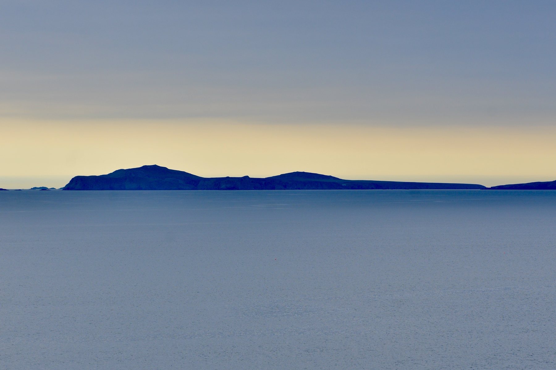 Calm sea at dusk, a low island silhouette on the horizon