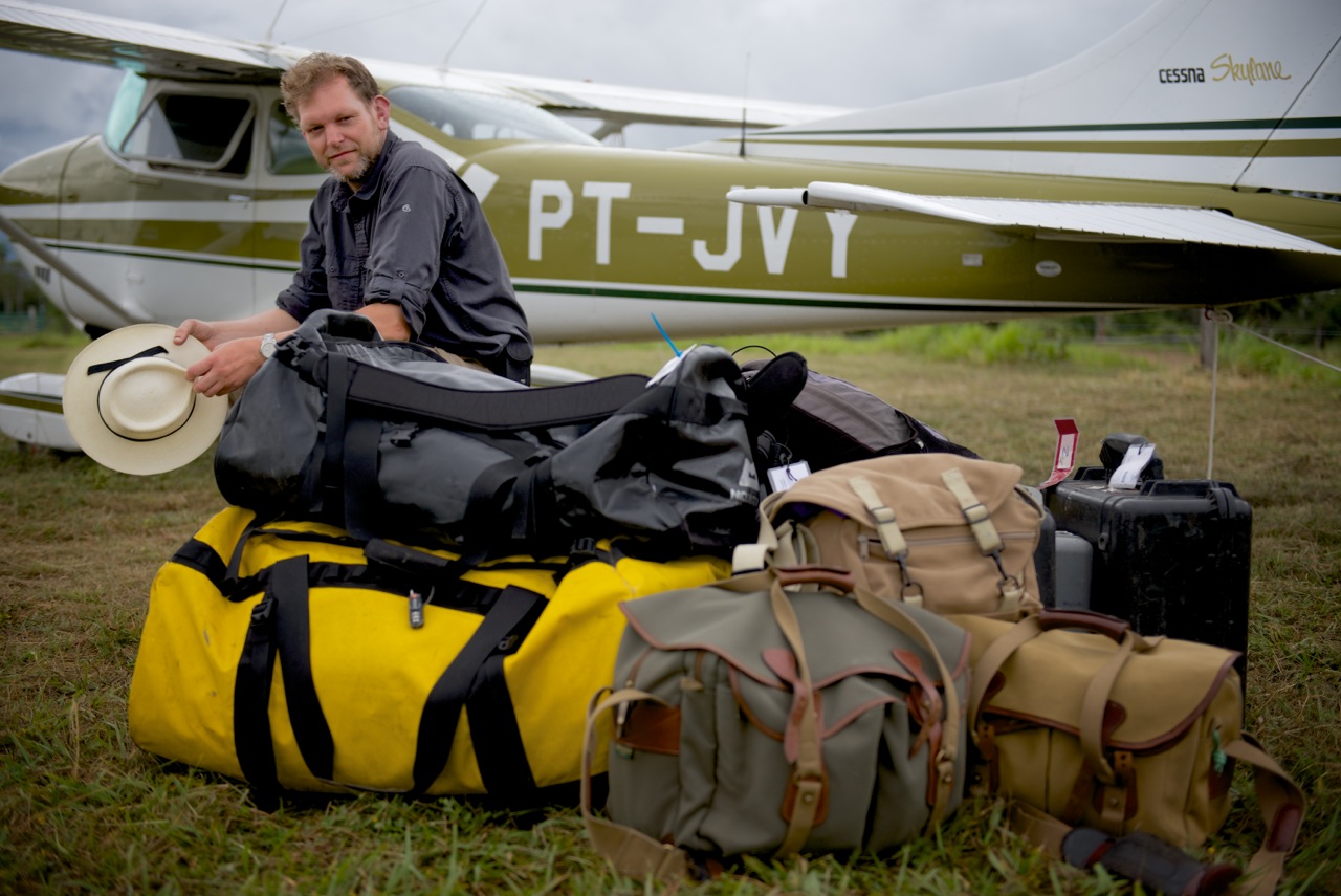 Adam White on location with his camera bags beside a light aircraft
